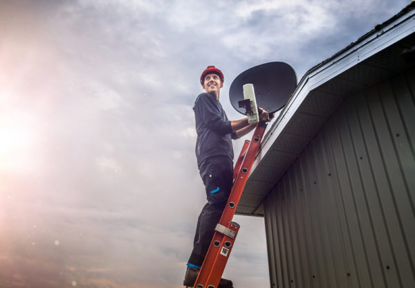Cheerful technician installing sattelite Cheerful young man standing on ladder and mounting residential satellite on roof.